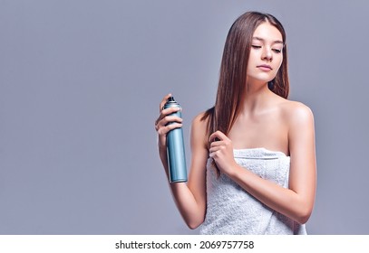 Woman With Clean Radiant Skin In A Towel Uses Hairspray Isolated On Gray Background.