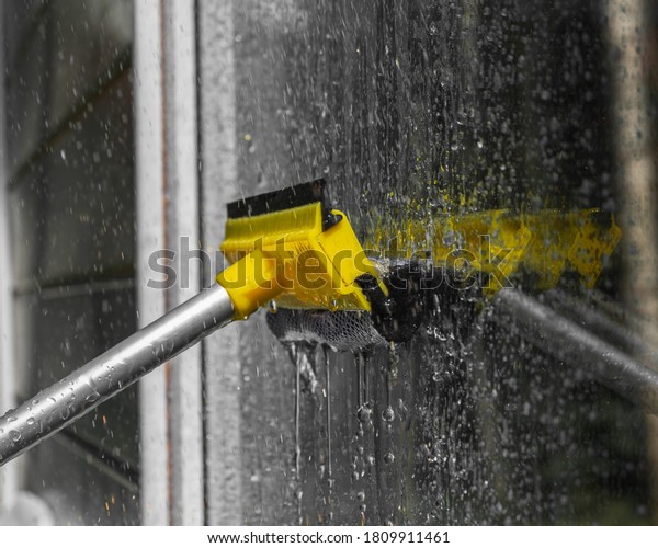 woman cleaner wiping window glass with a\
telescopic MOP outside a suburban private home, close-up, window\
washing concept with water\
splashes.