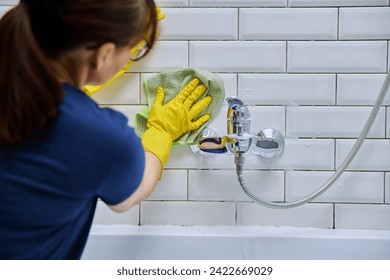 Woman cleaning bathroom, washing faucet, tile with professional cloth, foam cleaner