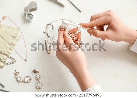 Woman cleaning beautiful bracelet with toothbrush on light background, closeup