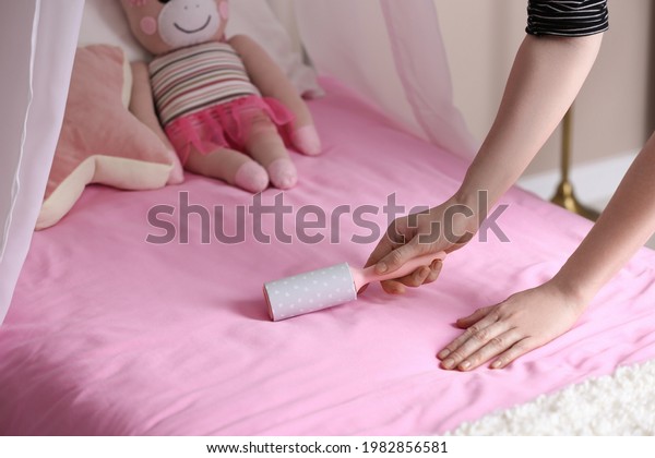 Woman\
cleaning bed with lint roller at home,\
closeup