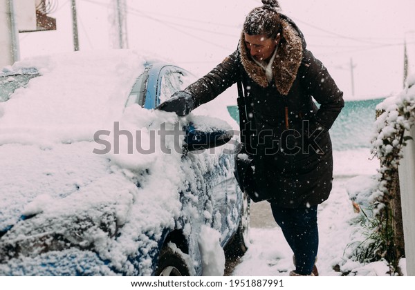 Woman cleaning car deep covered in snow during winter\
snowfall storm 