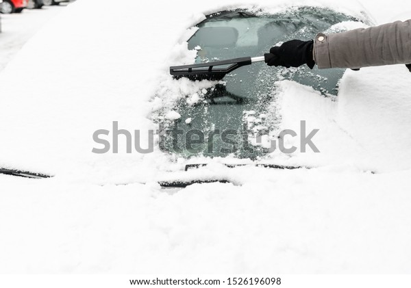 Woman cleaning car\
from the snow with brush. People in snowy cold weather in winter\
and transportation\
concept.