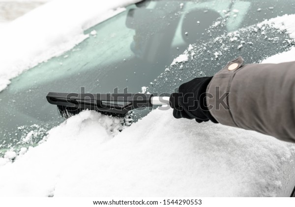 Woman cleaning car\
from the snow with brush. People in snowy cold weather in winter\
and transportation\
concept.