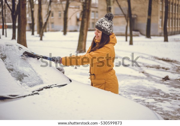 Woman cleaning car windshield of snow winter\
happy young scraper