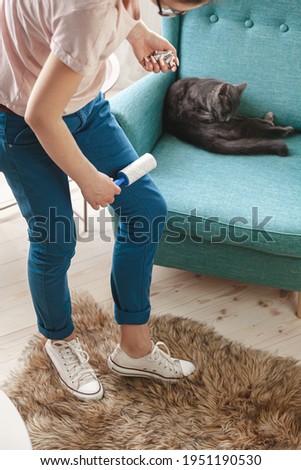 Woman cleaning clothes with sticky roller from cats hair, cleaning hair from pets