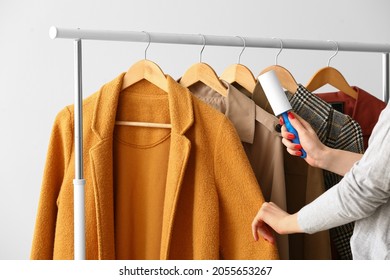 Woman cleaning coat with lint roller on light background