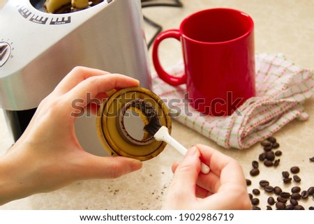 Woman cleaning coffee grinder with small brush