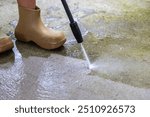 Woman cleaning concrete pavement using high pressure washer.