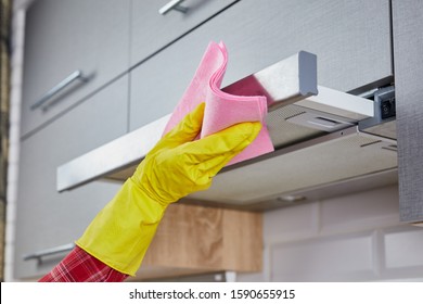 Woman Cleaning Cooker Hood With Rag In Kitchen. Close Up Of Female Hand In Rubber Protective Yellow Gloves Clean The Kitchen Metal Extractor Hood With Rag. Home, Housekeeping Concept