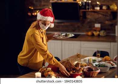 Woman Cleaning Dining Table After Christmas Dinner While Wearing Protective Face Mask Due To COVID-19 Pandemic.