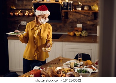 Woman Cleaning Dining Table After Christmas Dinner And Wearing Face Mask Due To Coronavirus Pandemic. 