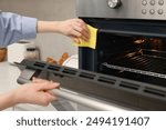 Woman cleaning electric oven with rag in kitchen, closeup