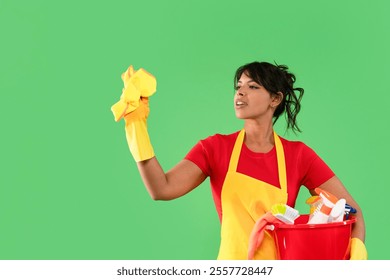 Woman cleaning with enthusiasm while holding a bucket of cleaning supplies against a green background - Powered by Shutterstock