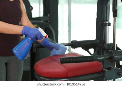 Woman Cleaning Exercise Equipment With Disinfectant Spray And Cloth In Gym, Closeup