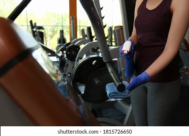 Woman Cleaning Exercise Equipment With Disinfectant Spray And Cloth In Gym, Closeup