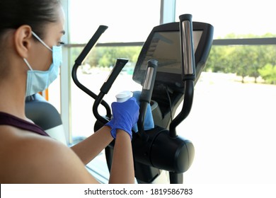 Woman Cleaning Exercise Equipment With Disinfectant Spray And Cloth In Gym