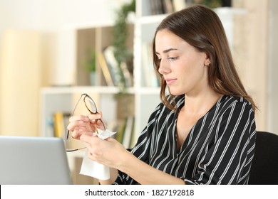 Woman cleaning eyeglasses with a tissue sitting in the living room at home - Powered by Shutterstock