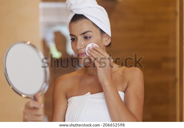 Woman cleaning face in\
bathroom 