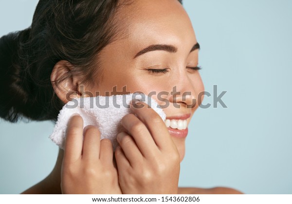 Woman cleaning facial skin with towel after washing\
face portrait. Beautiful happy smiling young asian female model\
wiping facial skin with soft towel, removing makeup. High quality\
studio shot
