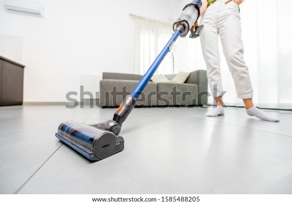 Woman cleaning floor with cordless vacuum cleaner\
in the modern white living room. Concept of easy cleaning with a\
wireless vacuum cleaner