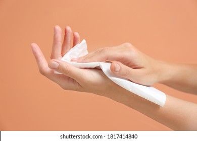 Woman cleaning hands with paper tissue on light brown background, closeup