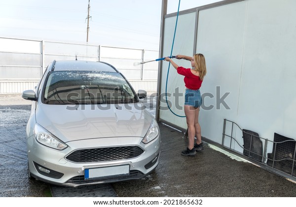 woman cleaning her auto with water jet with\
foam on car wash\
self-service