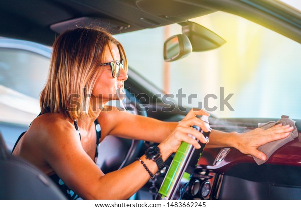 Woman\
cleaning her car cockpit using spray and microfiber cloth to clean\
and shine dashboard at self service car wash\
garage
