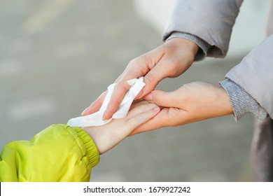 Woman Cleaning Kid Hands With Antiseptic Tissue Outdoors. Hands Hygiene. Female Using A Antibacterial Wet Napkin Wipe. Antiseptic Napkin To Prevent Spread Of Germs, Bacteria, Coronavirus And Virus.