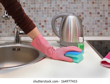 Woman Cleaning Kitchen Counter Top With Pink Glove And Sponge