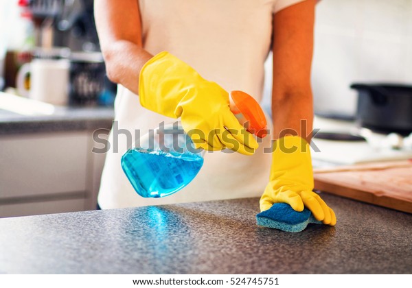 Woman cleaning the kitchen.\
Young housewife woman cleaning the kitchen with a blue cloth and\
spray. 
