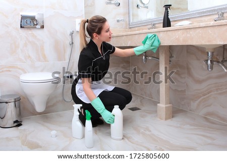 A woman in a cleaning lady's uniform can have a marble countertop in the bathroom. Plastic bottles of detergent on the floor. The concept of the hotel business.