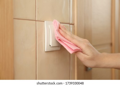 Woman Cleaning Light Switch With Rag Indoors, Closeup