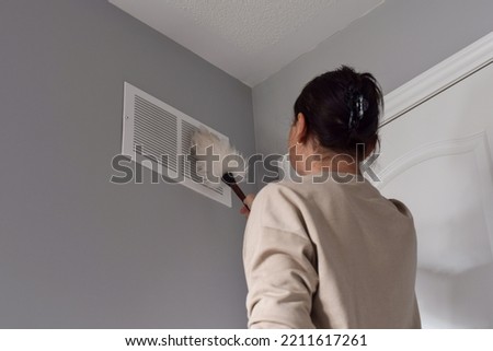 Woman cleaning return air vent with duster