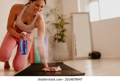 Woman Cleaning And Sanitizing Yoga Mat At Fitness Studio. Female In Home Gym Doing Sanitization On Fitness Mat Using Disinfectant Spray And Wipe.