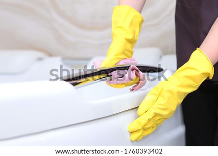 A woman in a cleaning service uniform and rubber gloves wipes the chrome surface.Cleanliness and hygiene in the bathroom.Unrecognizable photo. Only hand. Copy space.