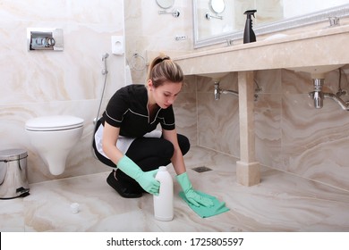 A Woman In A Cleaning Service Uniform Wipes The Marble Floor Tiles In An Expensive Hotel. Cleanliness And Disinfection In The Bathroom.