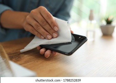 Woman Cleaning Smartphone With Wet Wipe At Wooden Table, Closeup