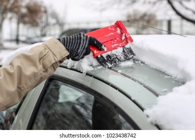 A Woman Cleaning The Snow Off The Car Roof In Winter Time.