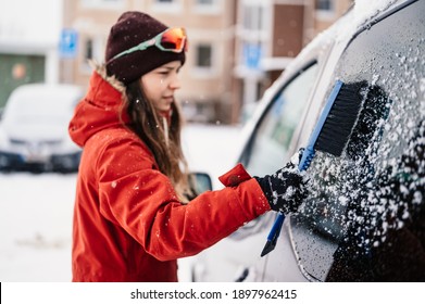 Woman Cleaning Snow Off His Car During Winter Snowfall. Scraping Ice. Winter Window Cleaning.