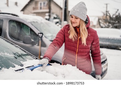 Woman Cleaning Snow Off His Car During Winter Snowfall. Scraping Ice. Winter Window Cleaning.