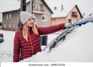 Woman Cleaning Snow Off His Car During Winter Snowfall. Scraping Ice. Winter Window Cleaning.