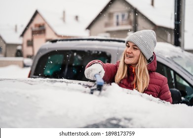 Woman Cleaning Snow Off His Car During Winter Snowfall. Scraping Ice. Winter Window Cleaning.