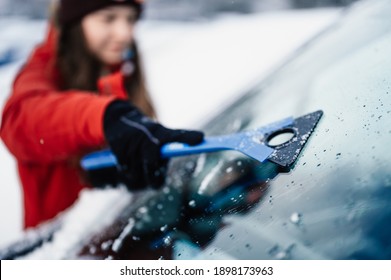 Woman Cleaning Snow Off His Car During Winter Snowfall. Scraping Ice. Winter Window Cleaning.