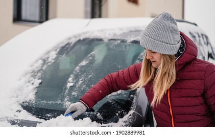 Woman Cleaning Snow Off His Car During Winter Snowfall. Scraping Ice. Winter Window Cleaning.