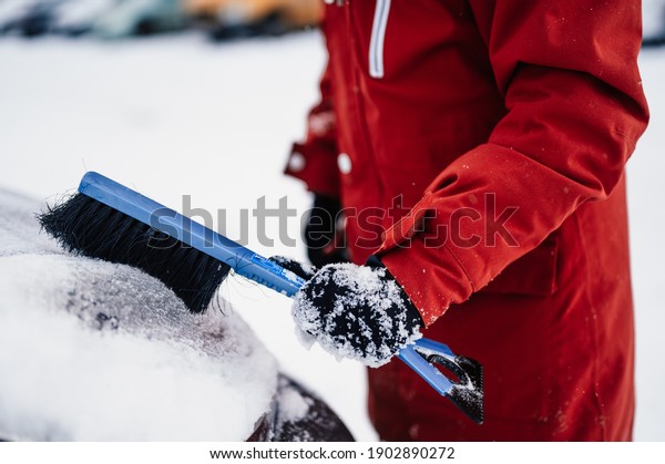 Woman cleaning snow off his car\
during winter snowfall. Scraping ice. Winter window\
cleaning.