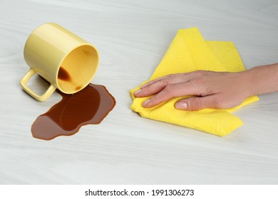 Woman Cleaning Spilled Coffee On White Wooden Table, Closeup