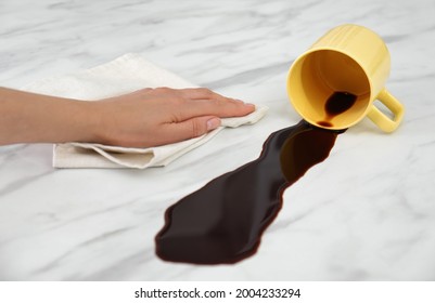 Woman Cleaning Spilled Coffee On White Marble Table, Closeup