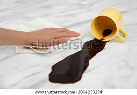 Woman cleaning spilled coffee on white marble table, closeup