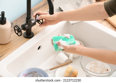 Woman With Cleaning Sponge Turning On Faucet In Kitchen, Closeup